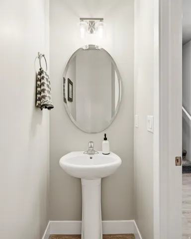 Pedestal sink featuring a chrome faucet, oval mirror, and a contemporary brushed nickel vanity light with clear glass shades