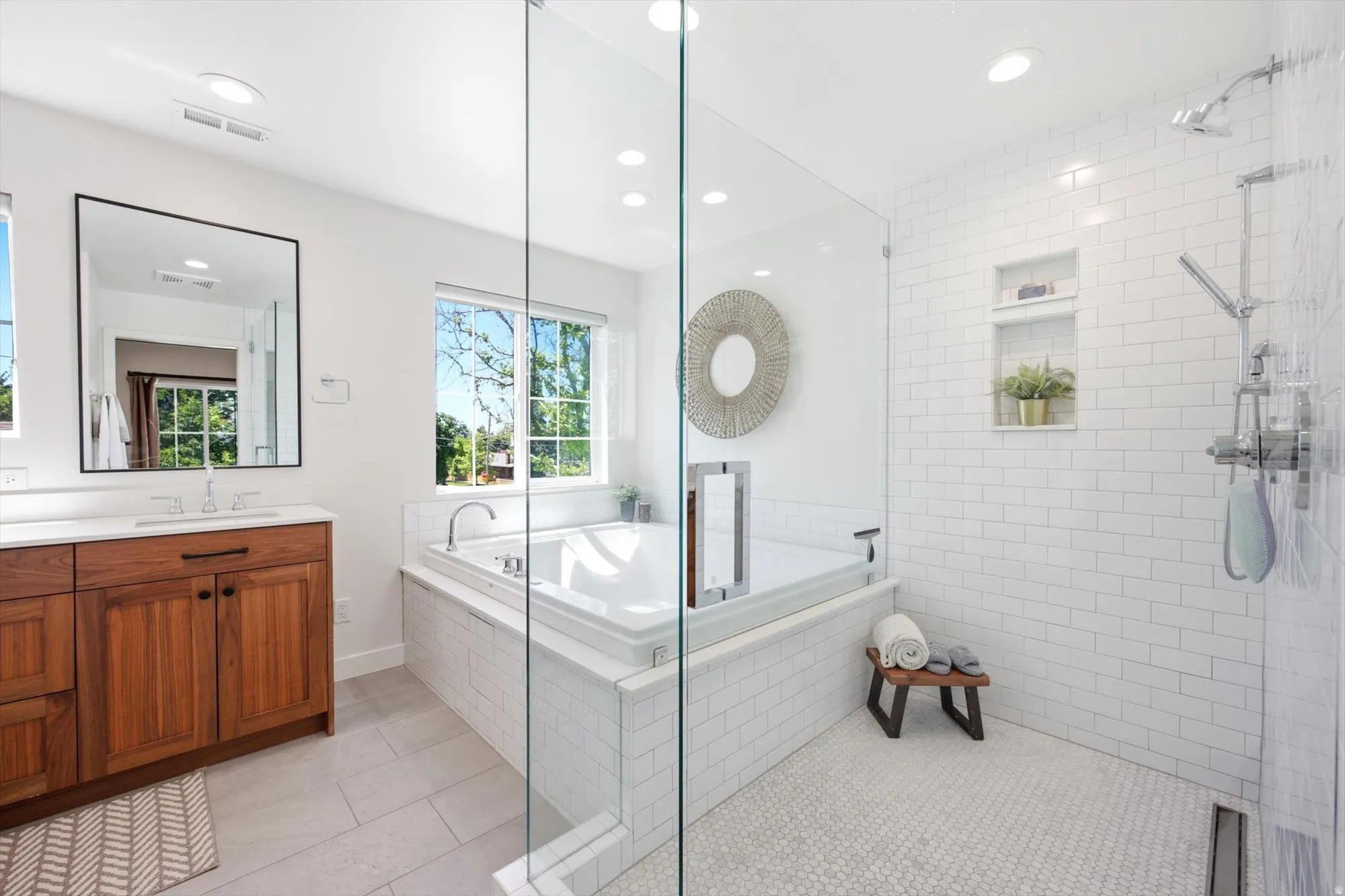 Bathroom featuring a built-in soaking tub, glass-enclosed shower with subway tile surround, and a wood-finish vanity with a white countertop