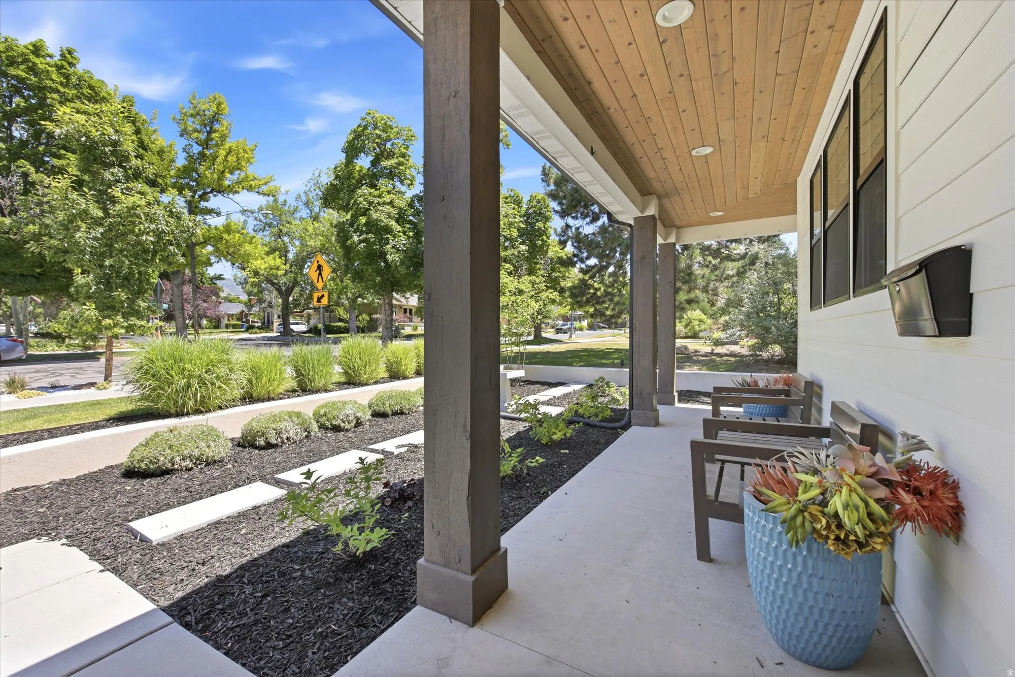 Covered front porch featuring a wood-finish ceiling with recessed lighting, substantial support columns, and concrete flooring