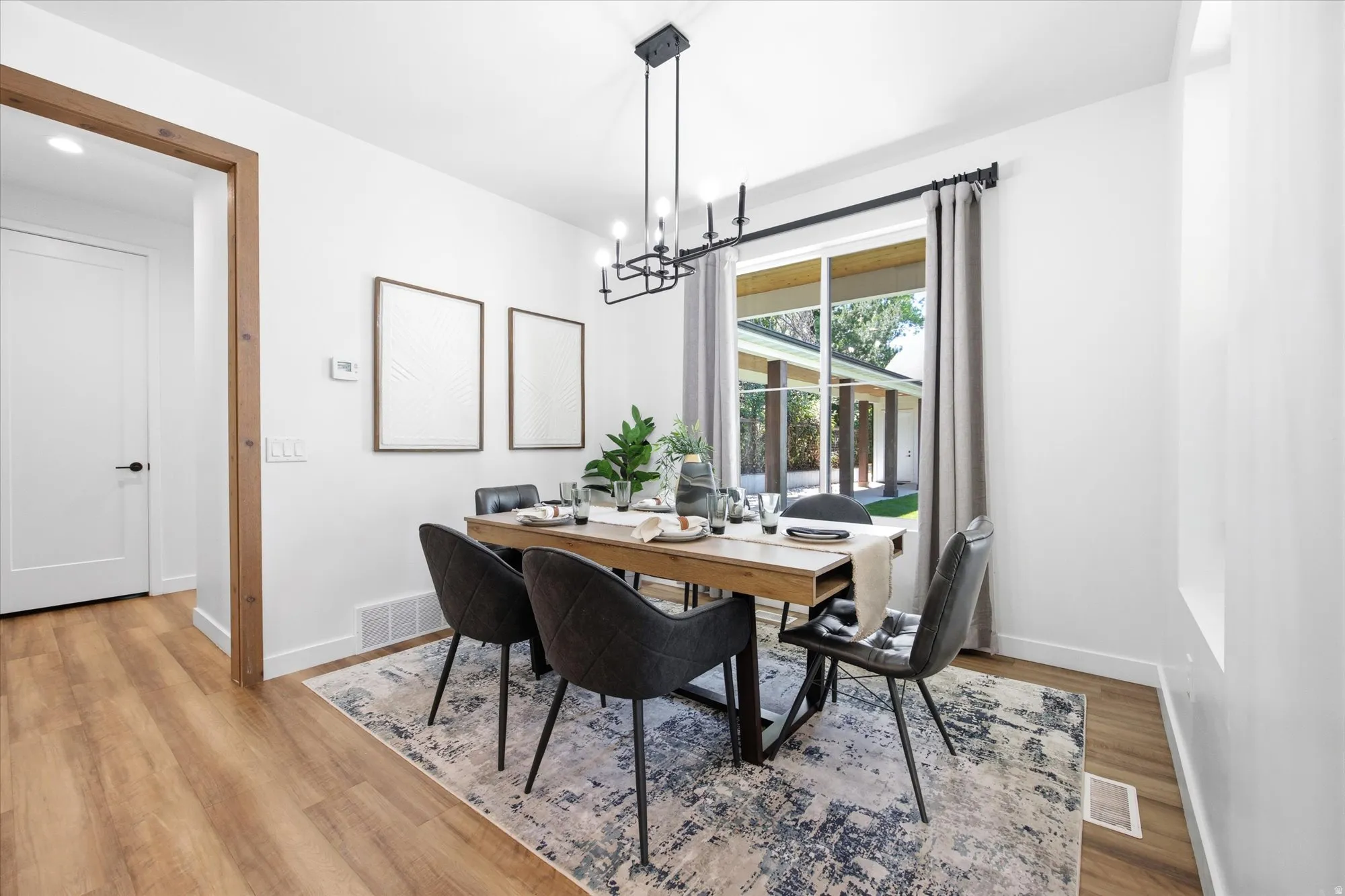 Dining area featuring wood-finish flooring, a contemporary chandelier, a large window with exterior views, and crisp white walls