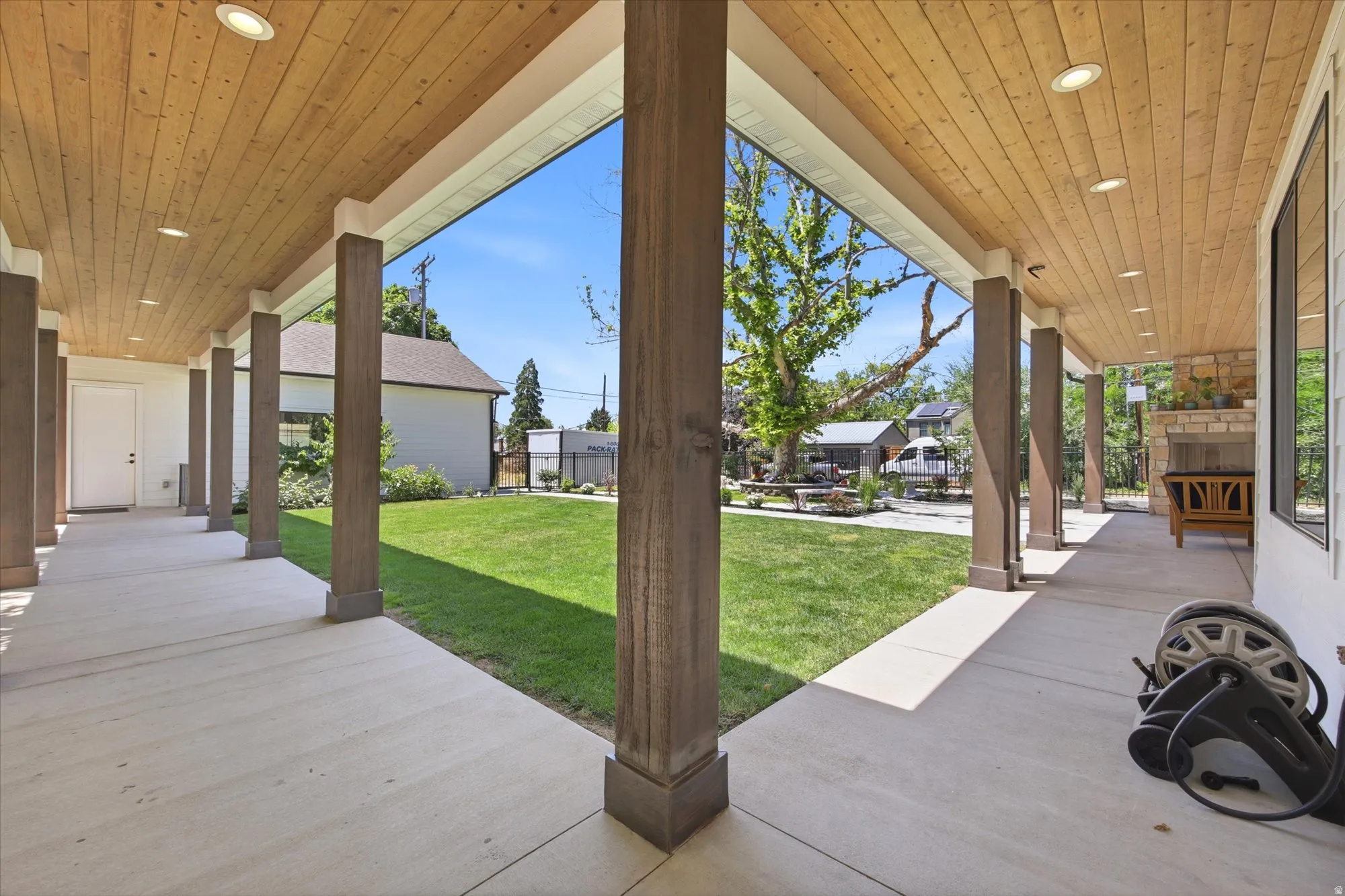Covered patio with recessed lighting, wood-finish ceiling, substantial support columns, concrete flooring, and a stone fireplace