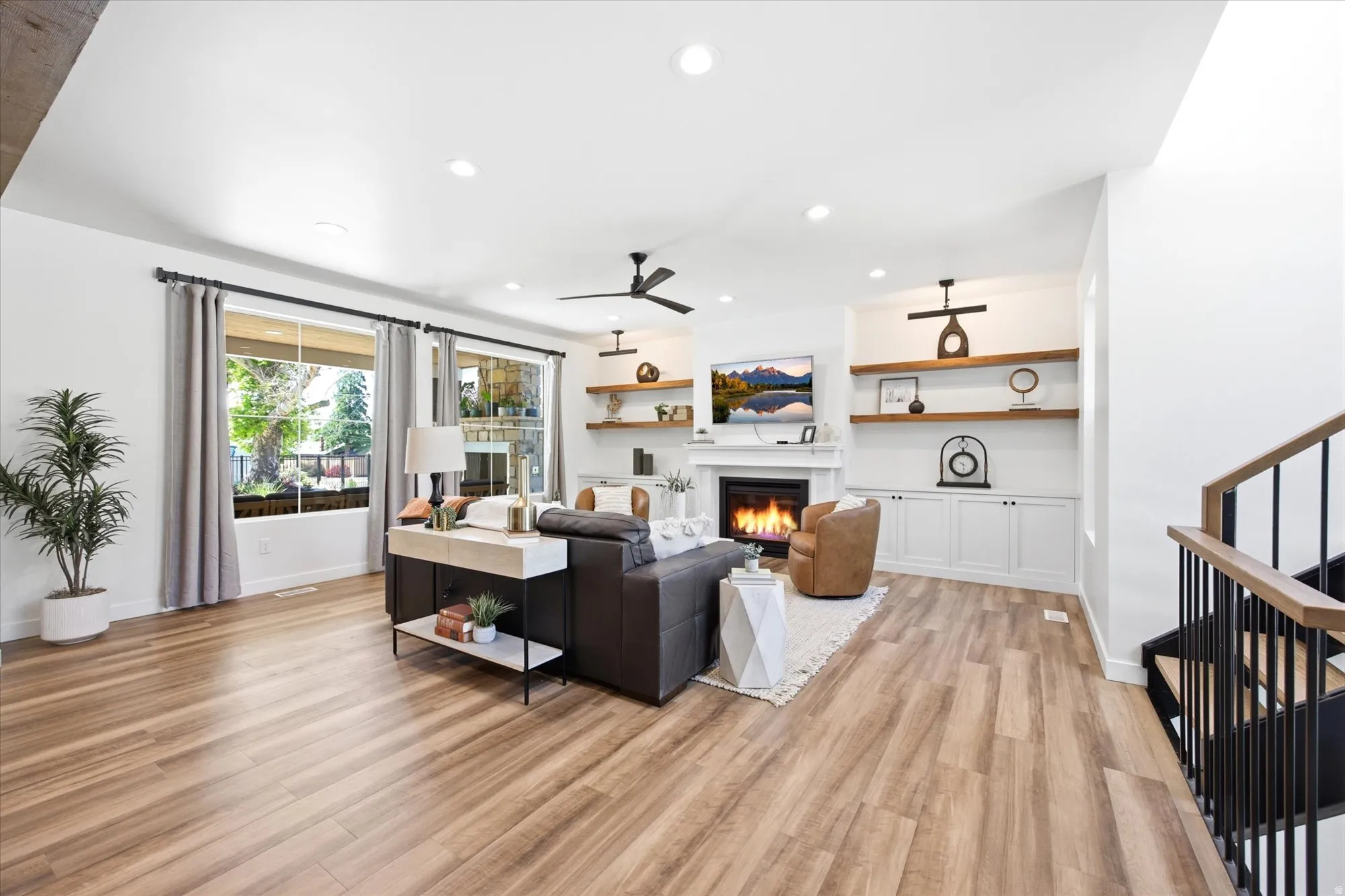 Spacious living area featuring wood-finish flooring, a fireplace with a white mantel, built-in cabinetry, and open shelving