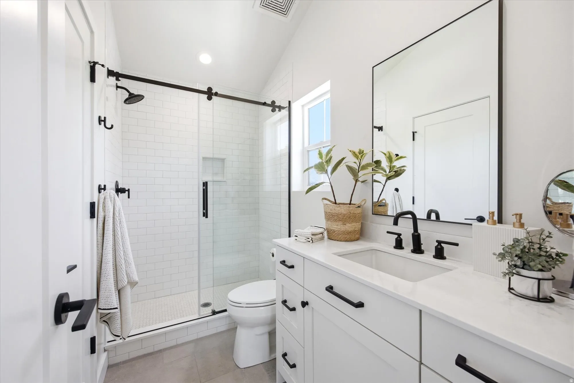 Sleek bathroom featuring a spacious walk-in shower with subway tile, a modern vanity with a white countertop and matte black fixtures, an expansive framed mirror, and a window for natural light