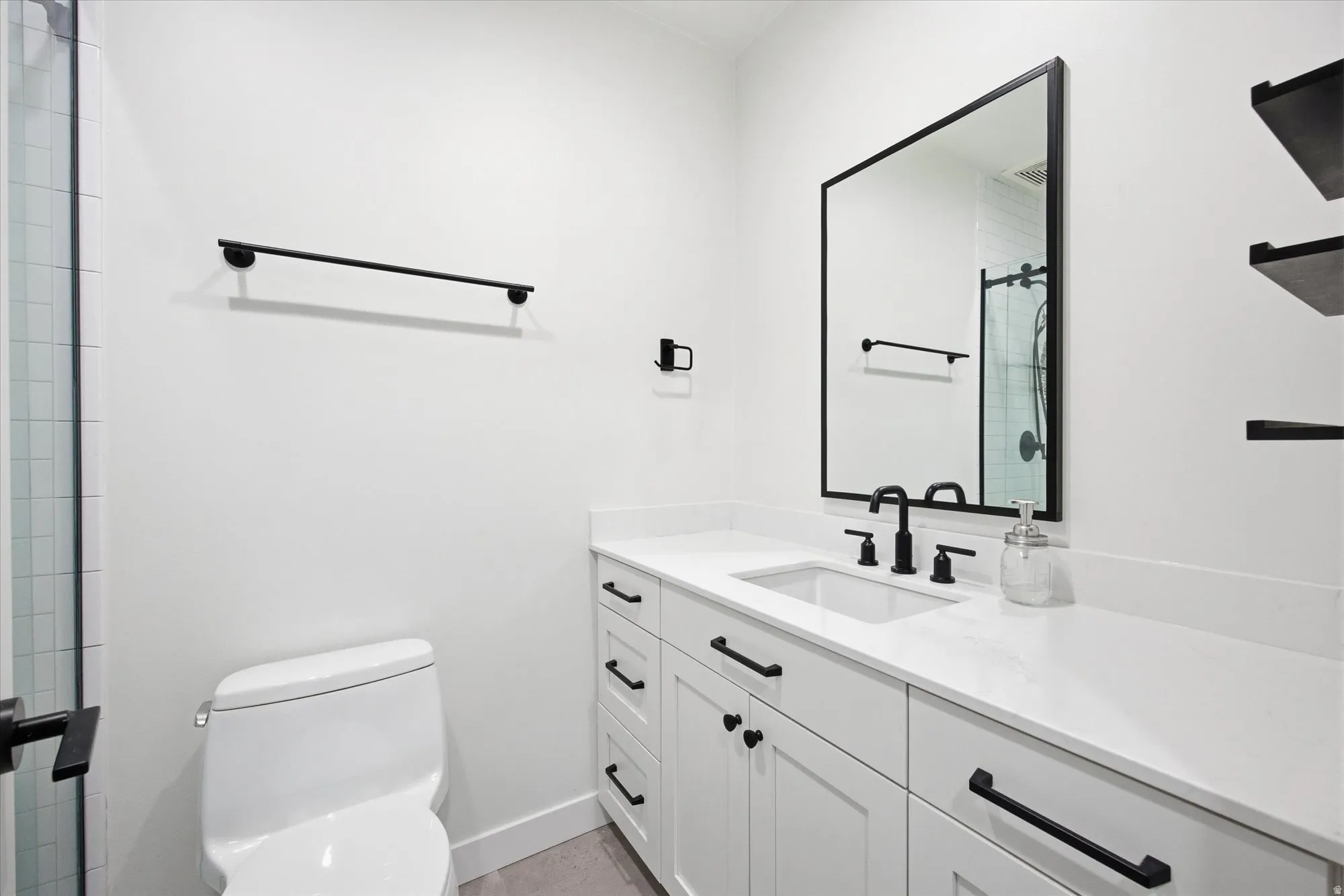Contemporary bathroom featuring a white vanity with integrated sink, black hardware, a framed rectangular mirror, and open shelving