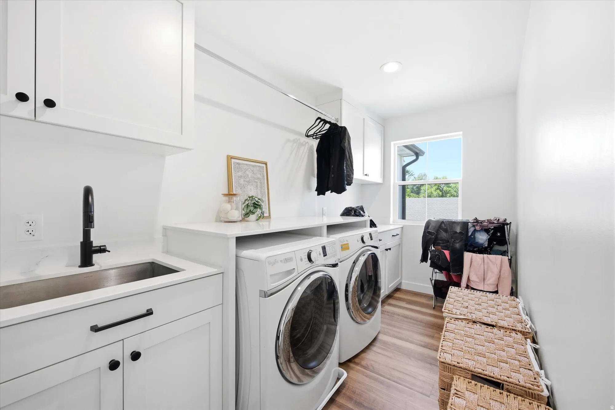 Dedicated utility room featuring wood-finish flooring, white cabinetry with black hardware, a stainless steel sink with a matte black faucet, and ample countertop space