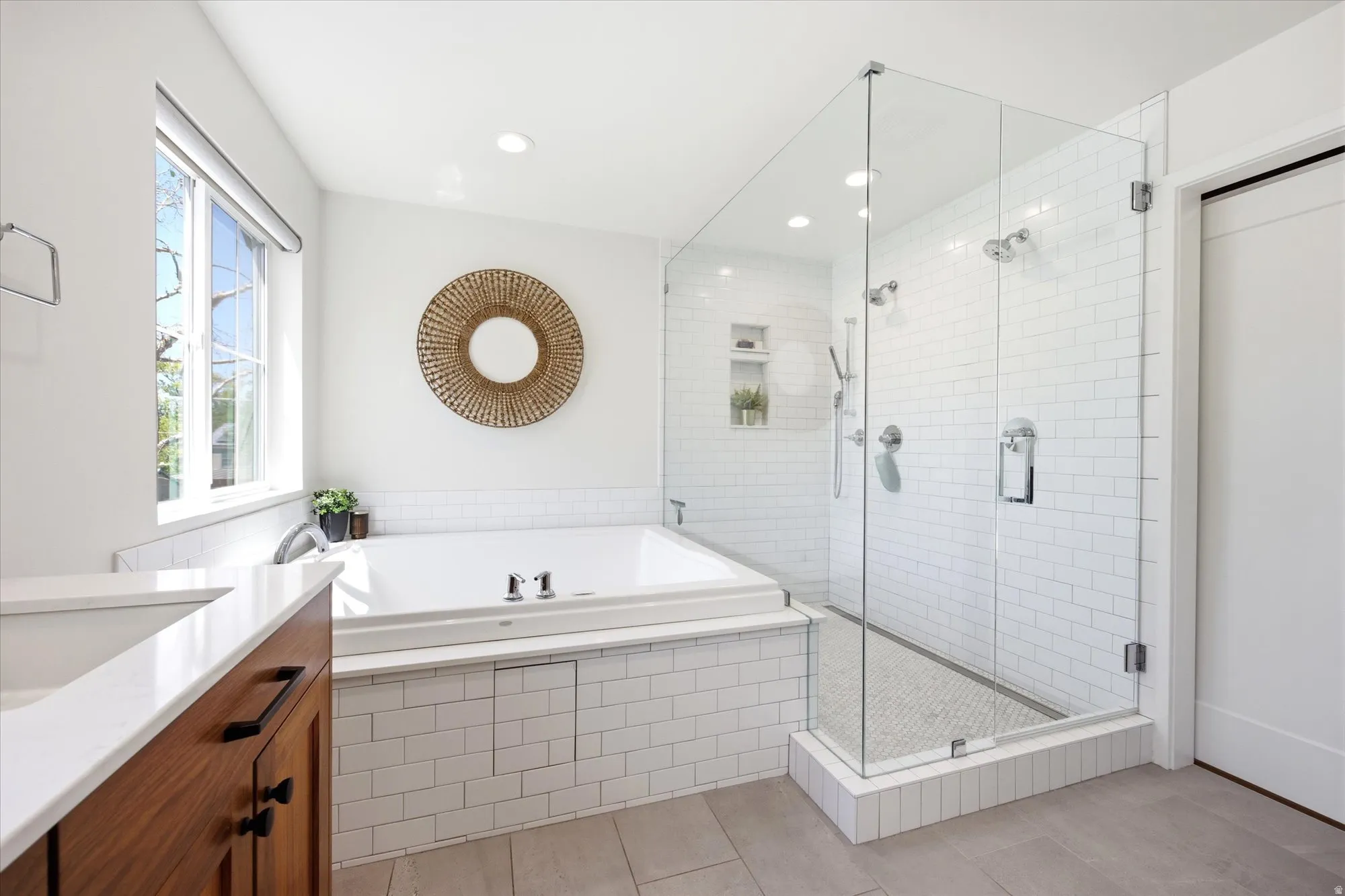 Bright bathroom featuring a large soaking tub with subway tile surround, a glass-enclosed shower with subway tile walls and mosaic tile floor, and wood-finish vanity with a white countertop