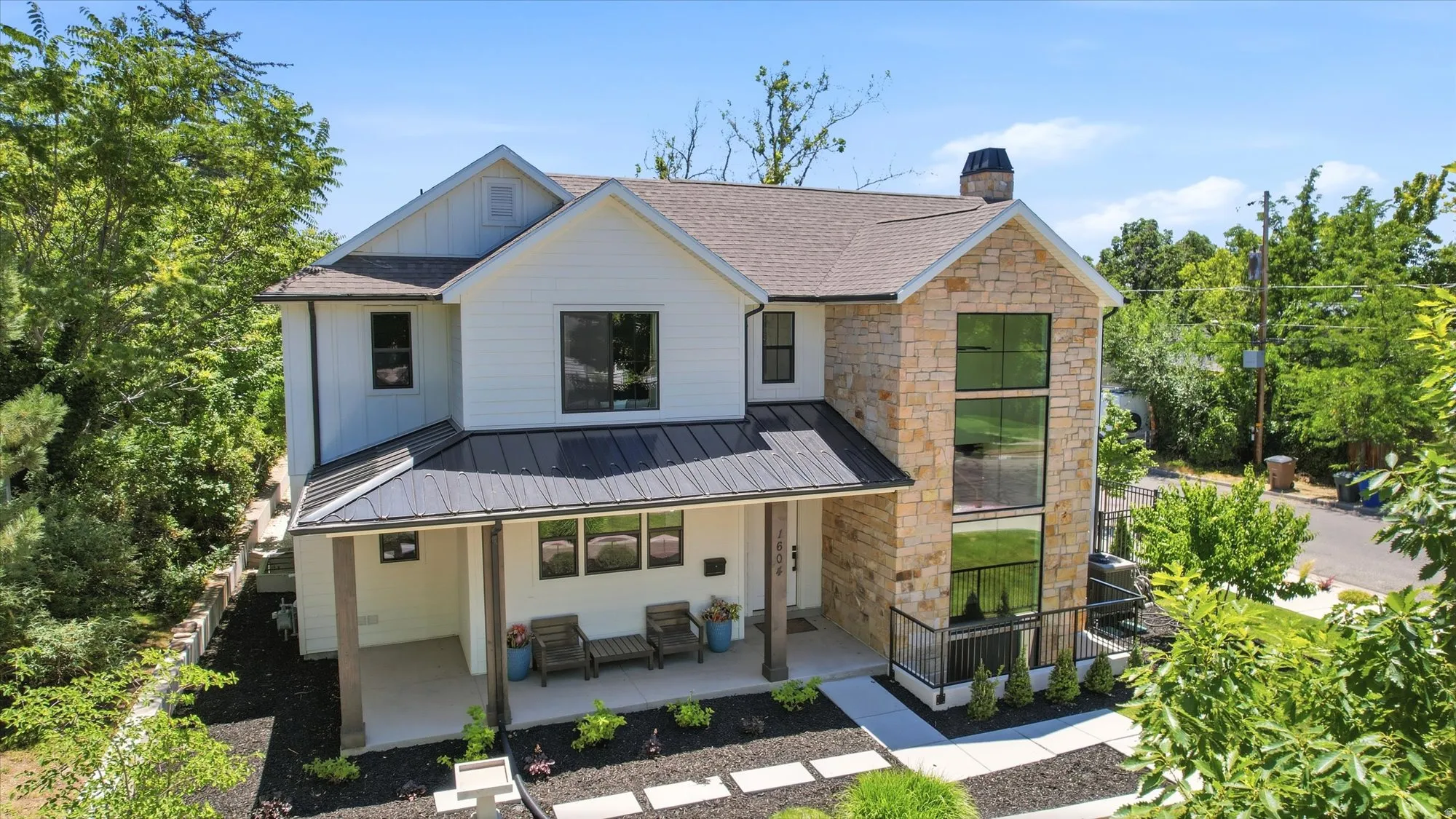Contemporary residence featuring a stone and white siding exterior with a dark metal roof