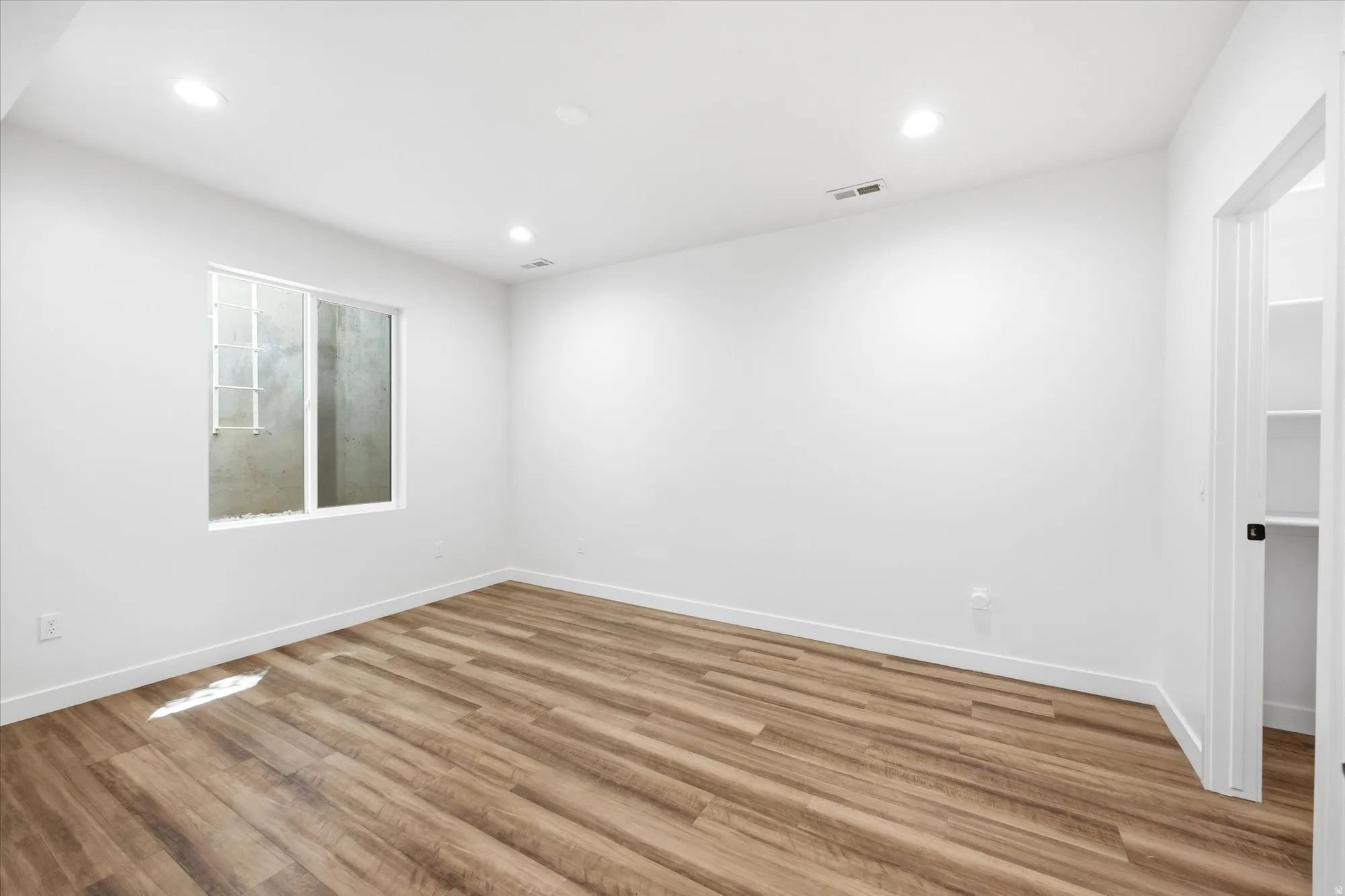 Spacious room featuring wood-finish flooring, recessed lighting, and a window with a security grate