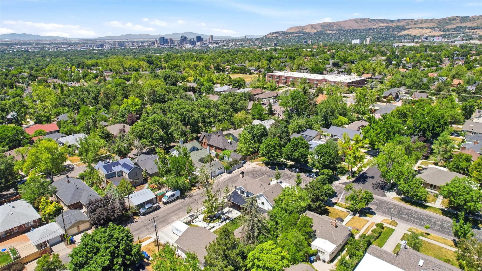 Expansive aerial landscape showcasing a residential neighborhood with abundant mature trees and mountainous terrain in the distance