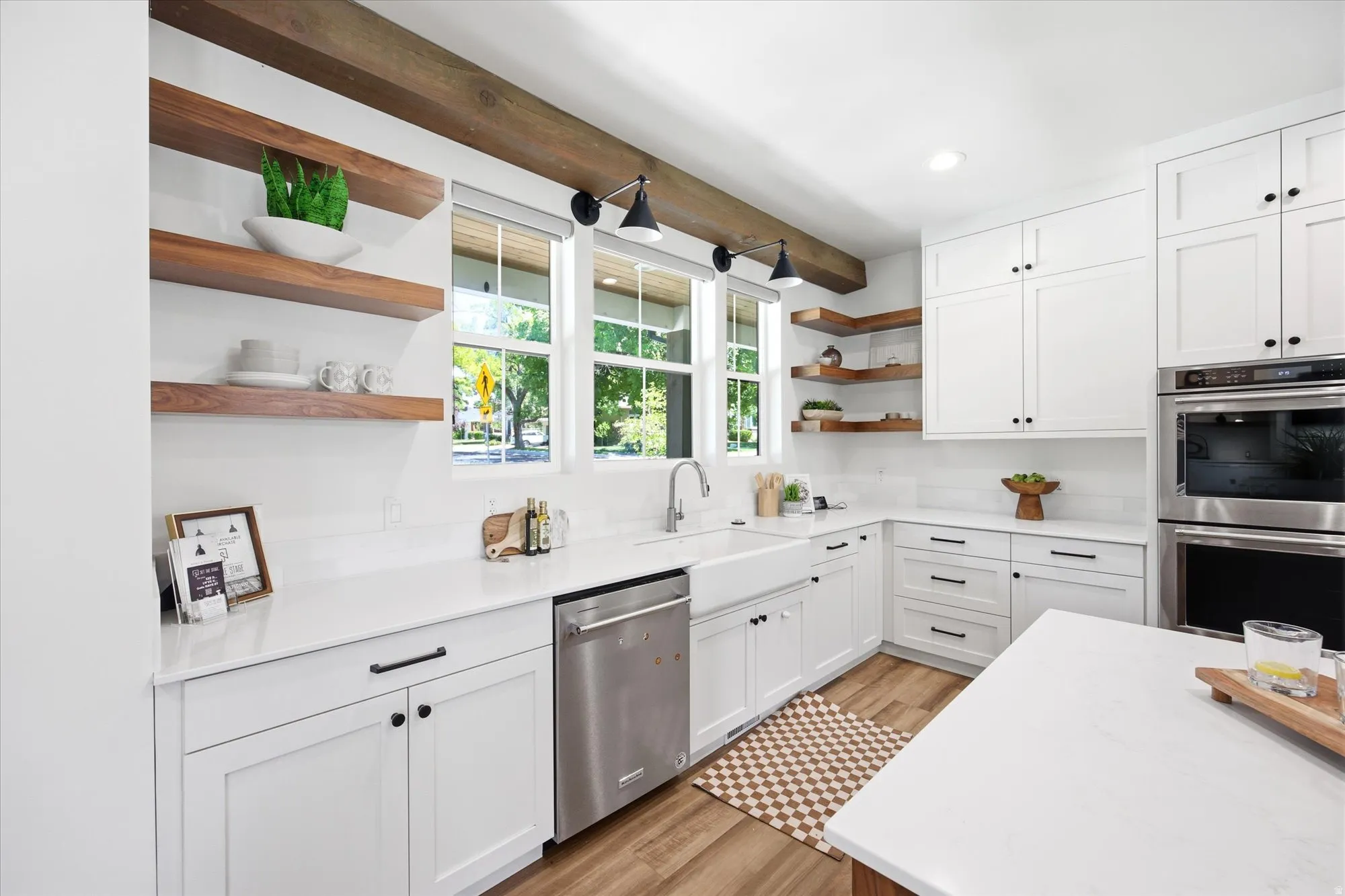 Modern kitchen featuring white cabinetry, quartz countertops, stainless steel appliances, wood-finish flooring, and exposed wood beams