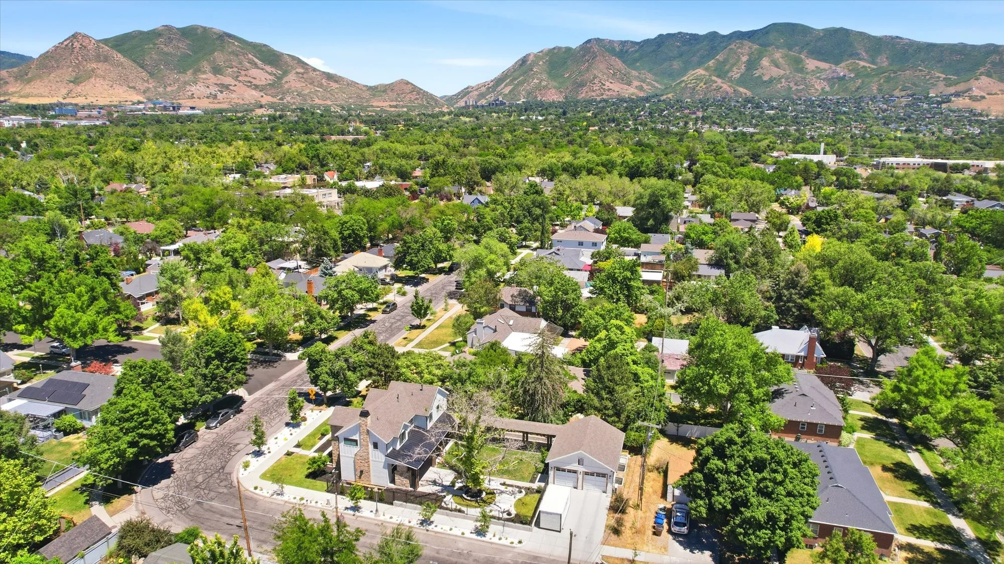 Aerial perspective showcasing a residential neighborhood with abundant mature trees and distant mountain ranges