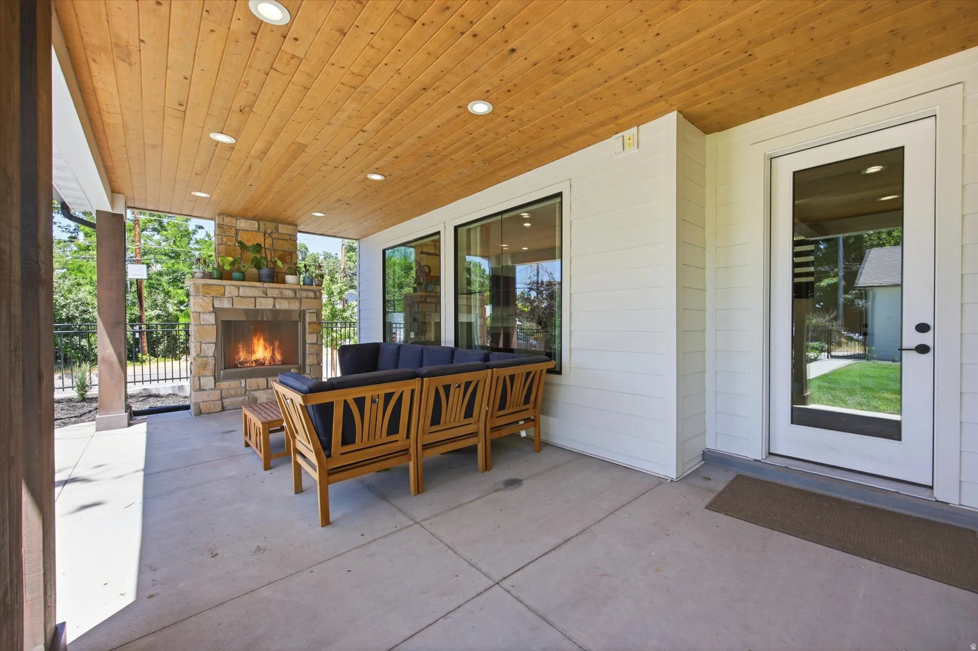 Covered patio featuring a stone fireplace, wood-plank ceiling with recessed lighting, and large glass windows