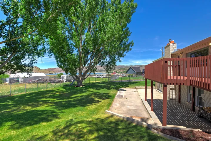 Expansive backyard featuring a manicured lawn, mature trees, and a red-stained wood deck with a privacy screen