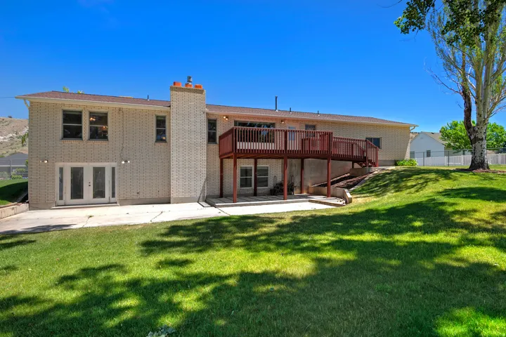 Rear exterior featuring a spacious elevated deck, brick facade, ground-level patio, and a large grassy yard