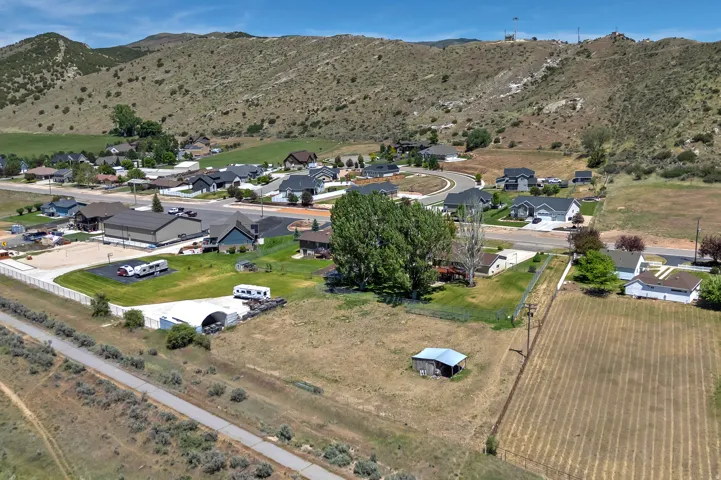 Expansive land parcel featuring open fields, a small outbuilding, and mature trees, surrounded by residential development and natural hills
