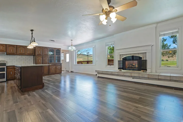 Spacious interior featuring wood-finish flooring, a kitchen island with stone-finish countertop, a fireplace with a tiled hearth and surround, and multiple windows providing natural light