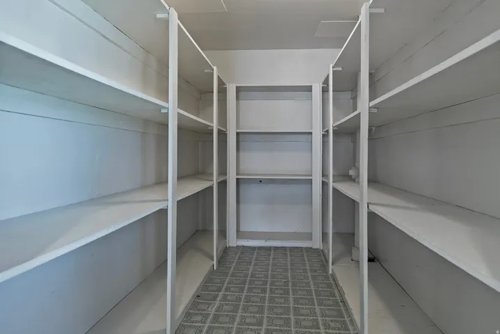 Walk-in pantry featuring extensive white shelving along three walls, providing abundant storage capacity