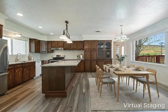 Open concept kitchen and dining area featuring wood-finish flooring, a kitchen island with a light-toned countertop, dark wood cabinetry, and a bright window above the sink