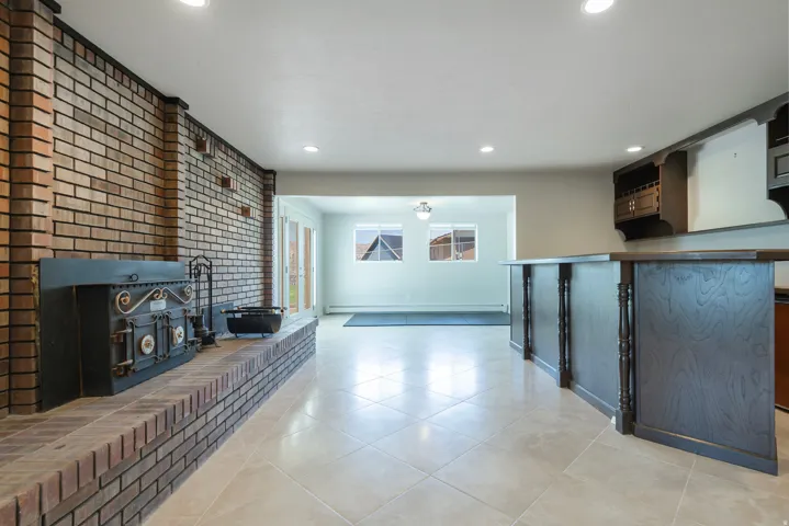Expansive tiled flooring spans this versatile space, featuring a prominent brick fireplace with a decorative insert