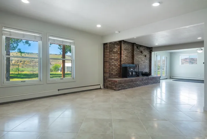 Expansive room featuring large windows, light-toned tile flooring, a brick fireplace with a hearth, recessed lighting, and French doors leading outdoors