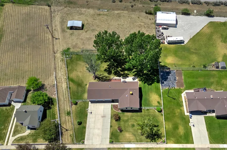 Aerial property view featuring a large green lawn, mature shade trees, a concrete driveway, and a fenced perimeter