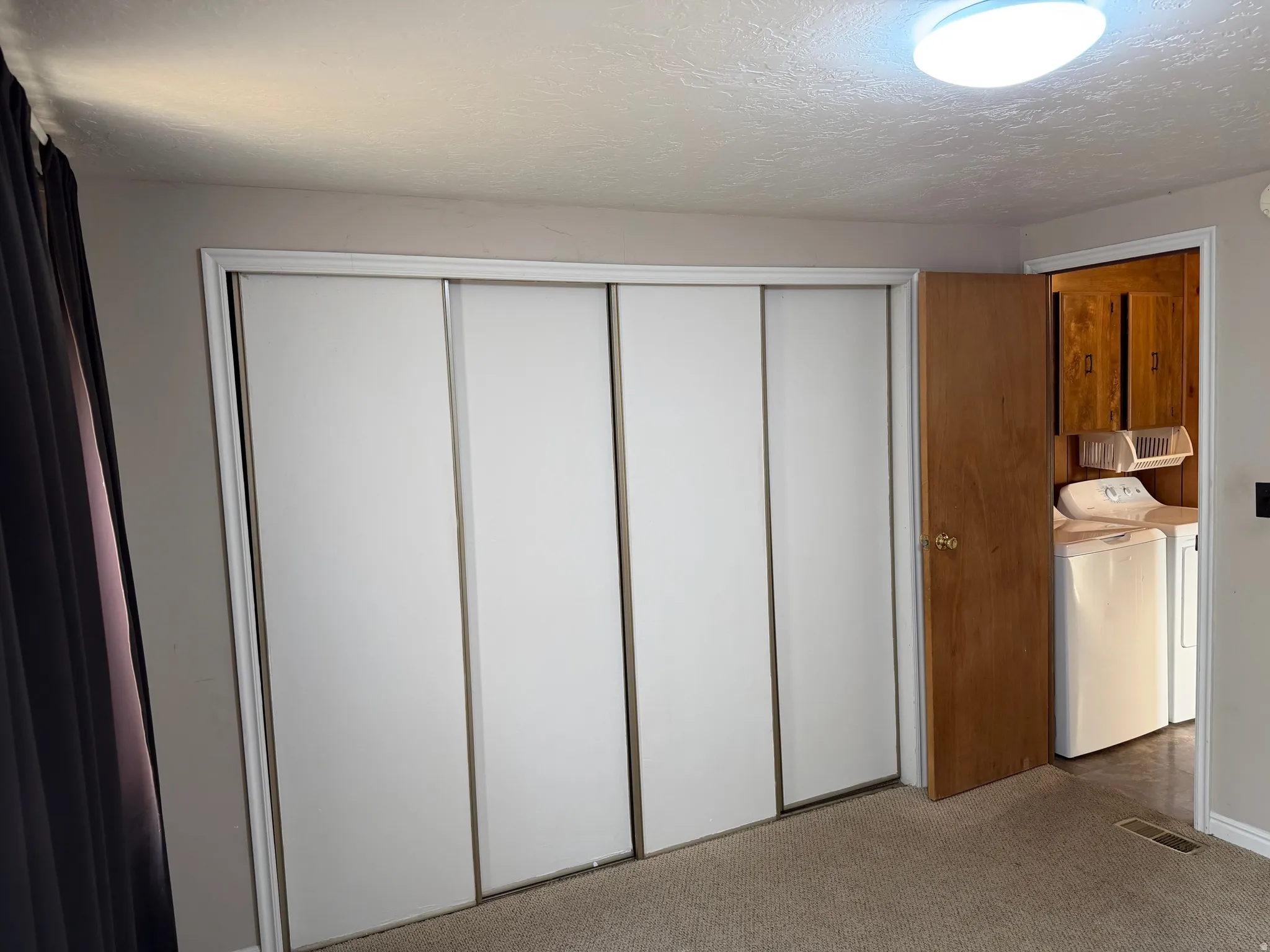 Wall-to-wall sliding closet doors with white panels, carpeted flooring, and a flush-mount ceiling light