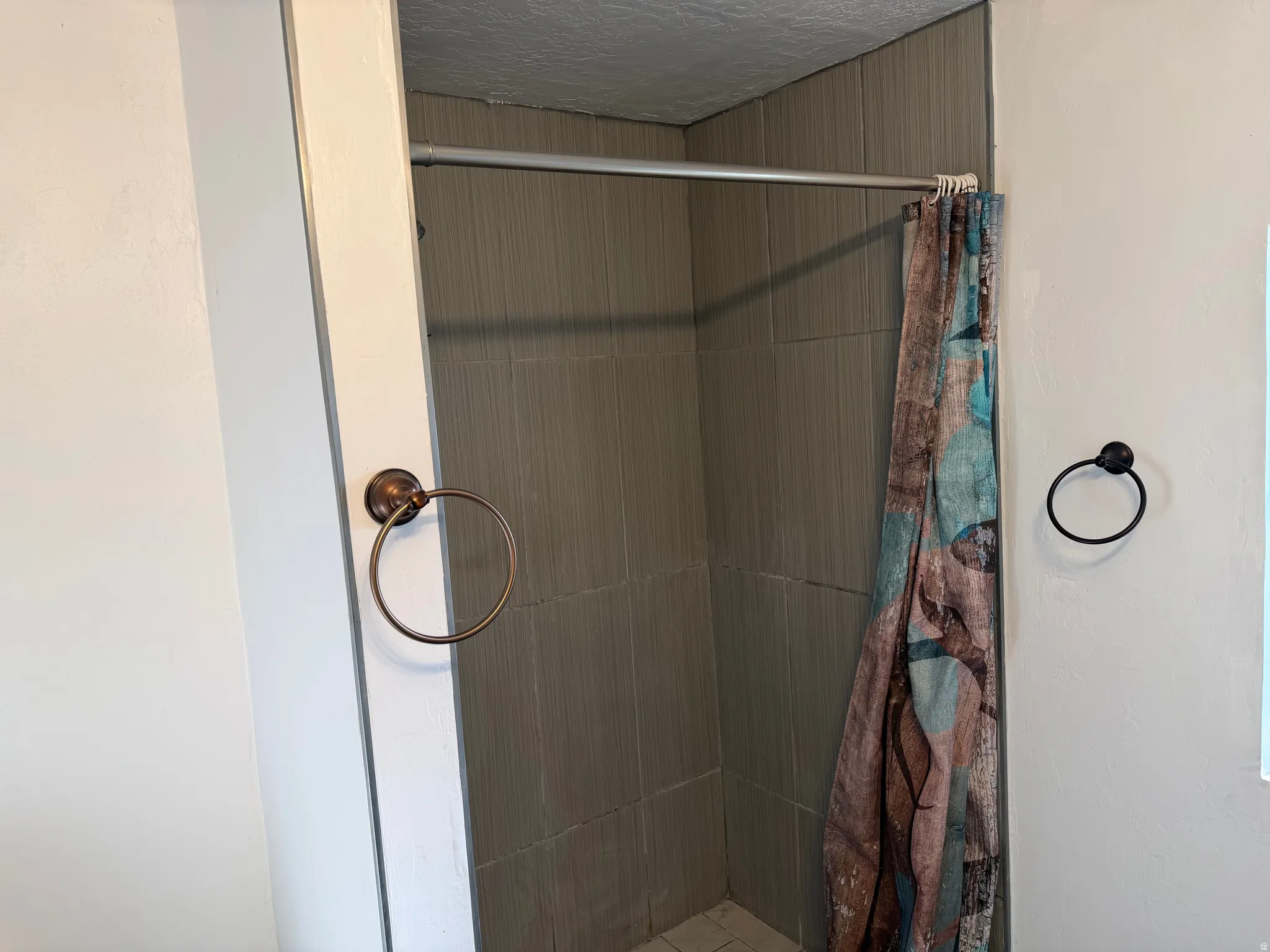 Shower enclosure featuring neutral-toned tile walls and a white tiled floor
