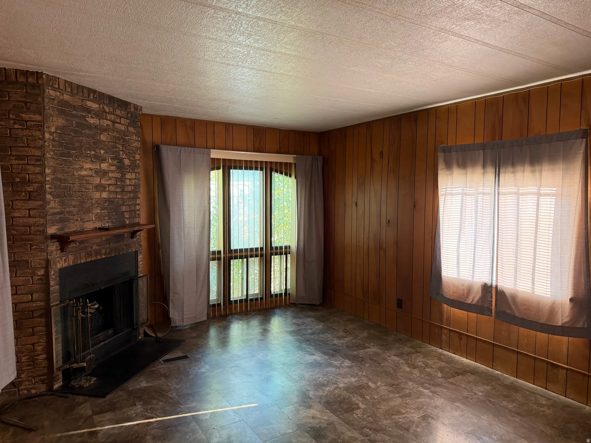 Living area featuring a brick fireplace with a wood mantle, wood-finish flooring, wood paneling, and multiple windows for natural light