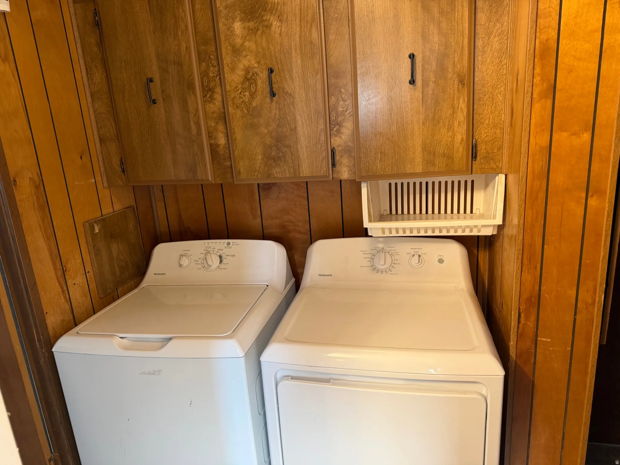 Dedicated laundry area featuring wood-paneled walls and overhead cabinetry