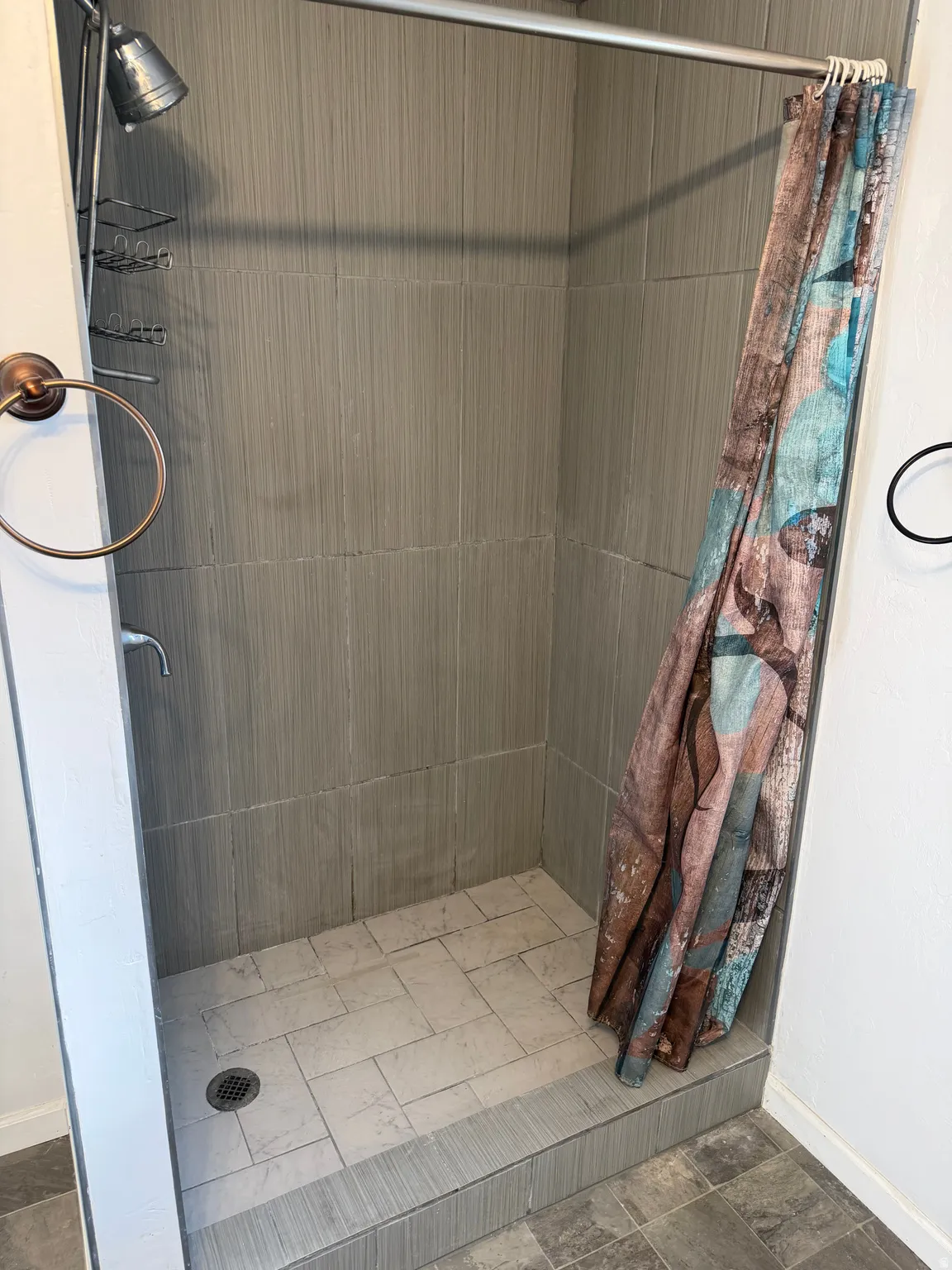 Tiled shower stall featuring a shower head, wall-mounted faucet, and built-in shelving