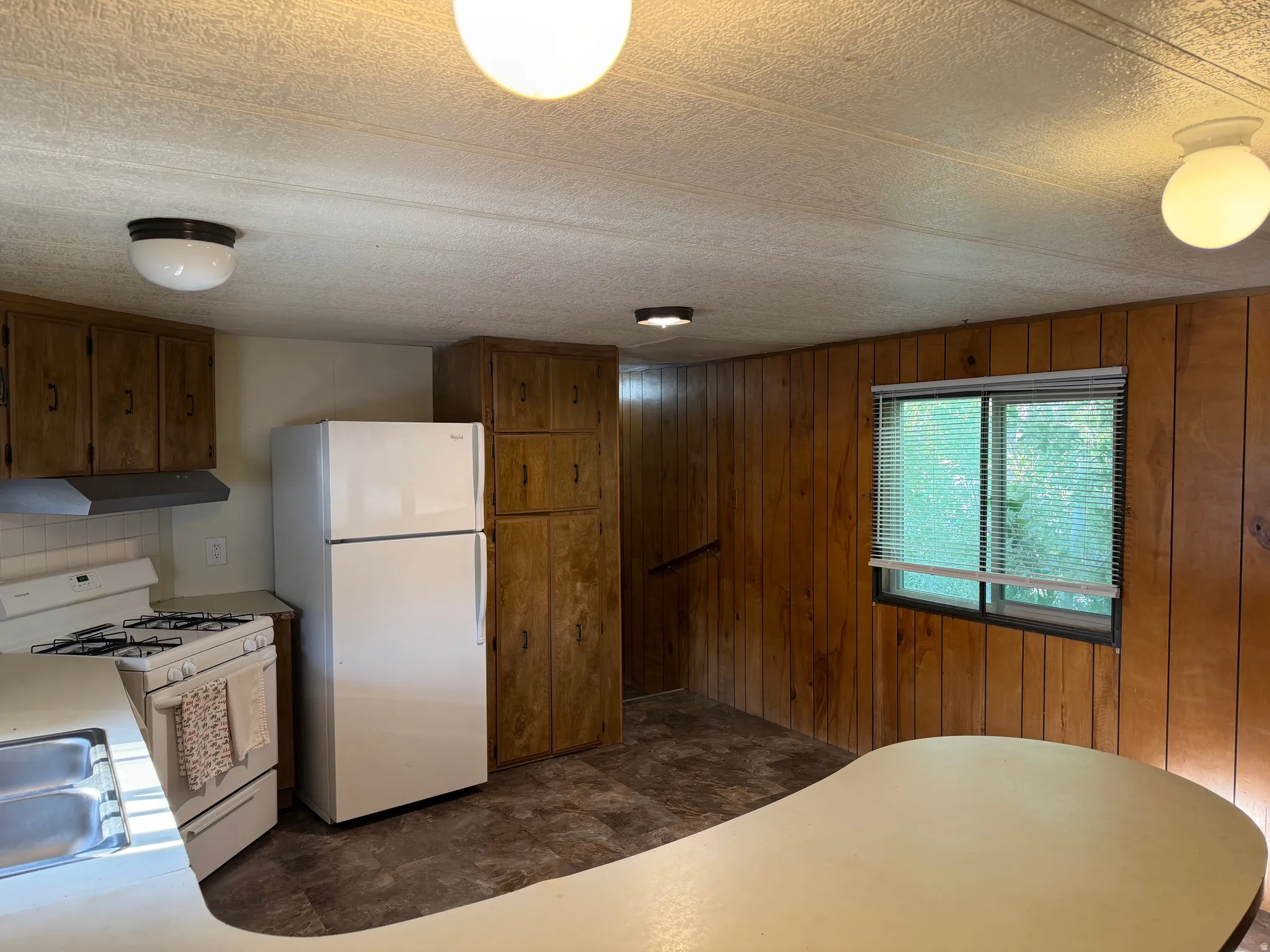 Functional kitchen space featuring wood-finish cabinetry, a white refrigerator, a white range with a range hood, and a built-in countertop