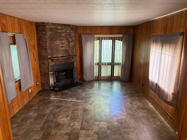 Living area featuring a corner brick fireplace with a metal insert and hearth, wood paneling, patterned flooring, and multiple windows