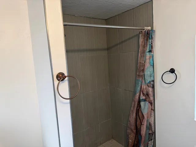 Shower enclosure featuring neutral-toned tile walls and a white tiled floor