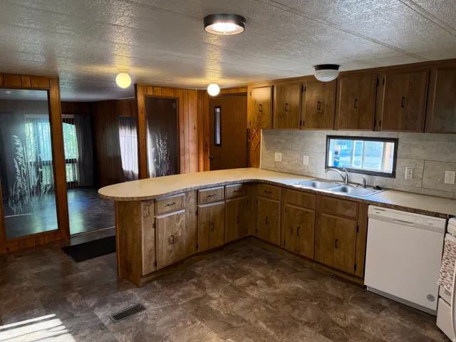 Kitchen featuring wood-finish cabinetry, a double basin stainless steel sink, and a white built-in dishwasher