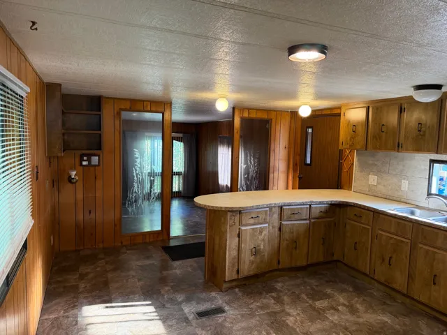 Kitchen featuring a U-shaped countertop with an integrated sink, wood-finish cabinetry, and a light-toned tile backsplash