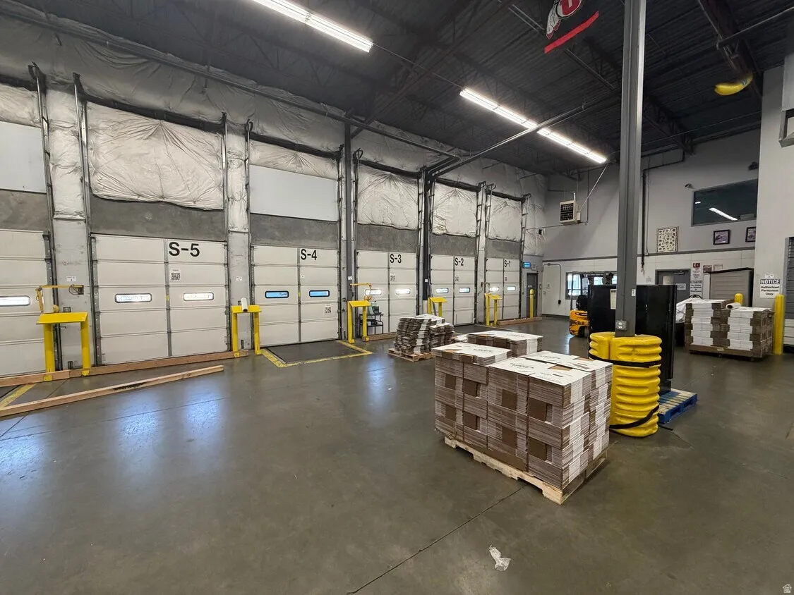 Industrial warehouse interior featuring multiple loading dock doors, concrete flooring, high ceilings with exposed ductwork, and fluorescent strip lighting