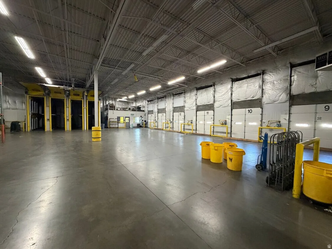 Spacious industrial interior featuring extensive concrete flooring, multiple overhead dock doors, and high ceilings with exposed metal trusses