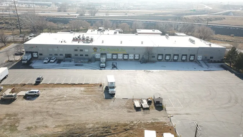 Industrial building featuring multiple loading docks, a large paved parking area, and an expansive gravel lot