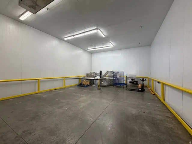 Spacious commercial interior featuring white panel walls, concrete flooring, fluorescent overhead lighting, and a yellow safety railing system