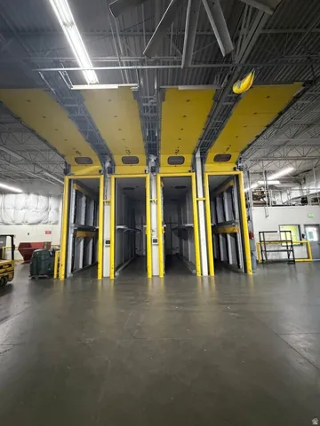 Industrial interior featuring multiple overhead doors with yellow panels, high ceilings, exposed structural beams, and concrete flooring