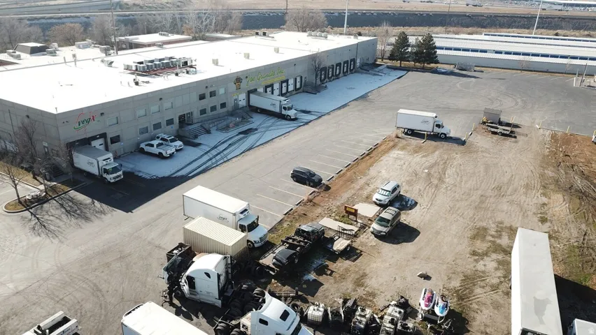 Commercial building featuring multiple loading docks, a large asphalt parking area, and an expansive gravel lot