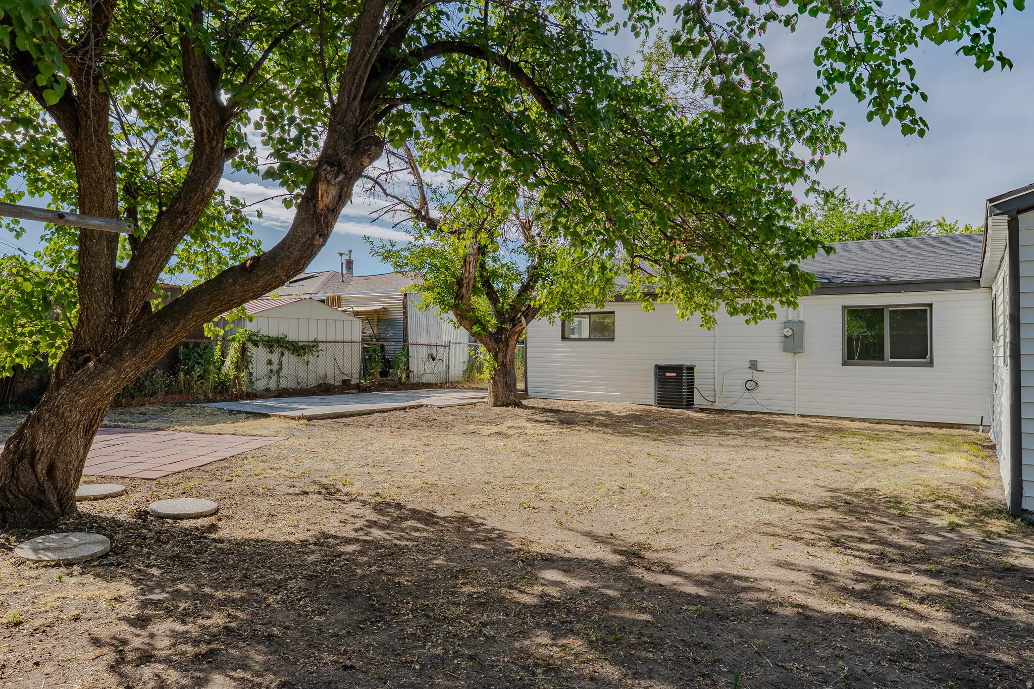 Spacious backyard featuring mature trees, a concrete patio area, and red brick pavers