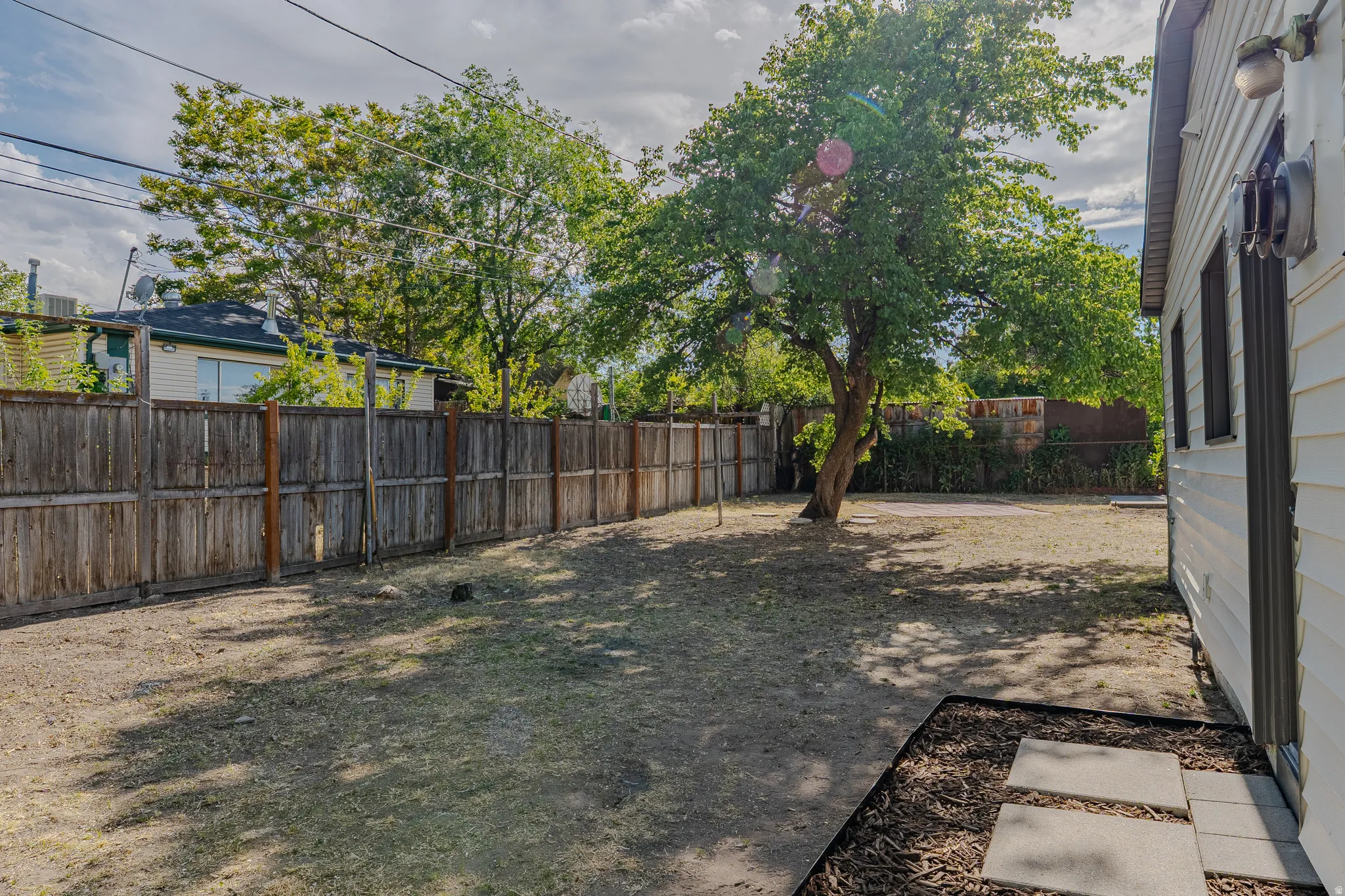 Expansive backyard featuring a mature tree, wood privacy fencing, and a concrete paver walkway alongside the property
