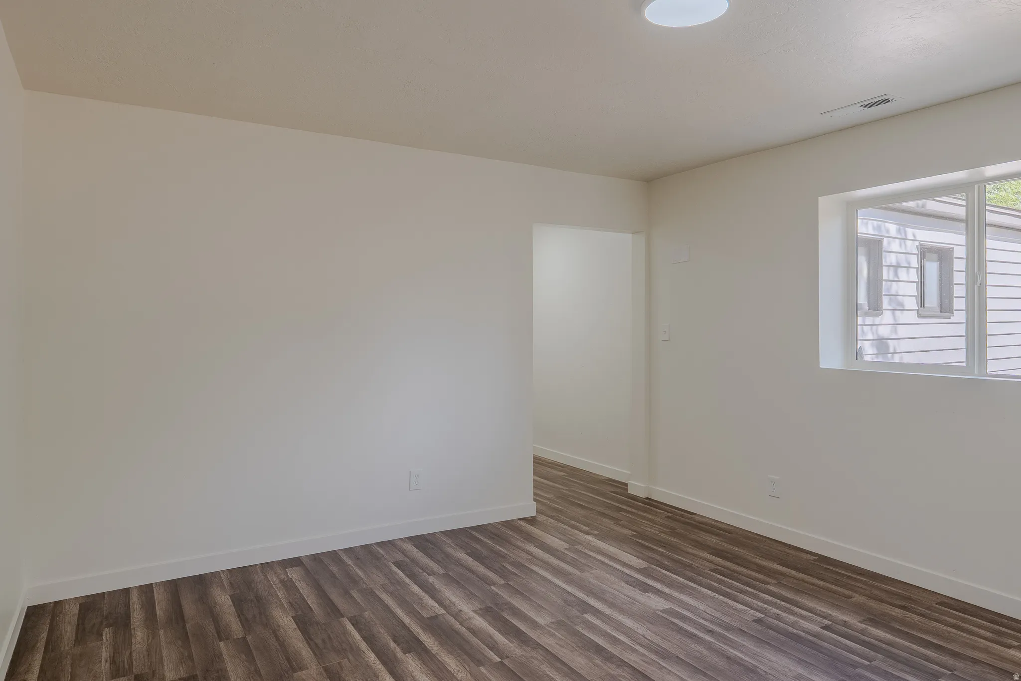 Spacious room featuring wood-finish flooring, white walls, and a contemporary flush-mount ceiling light