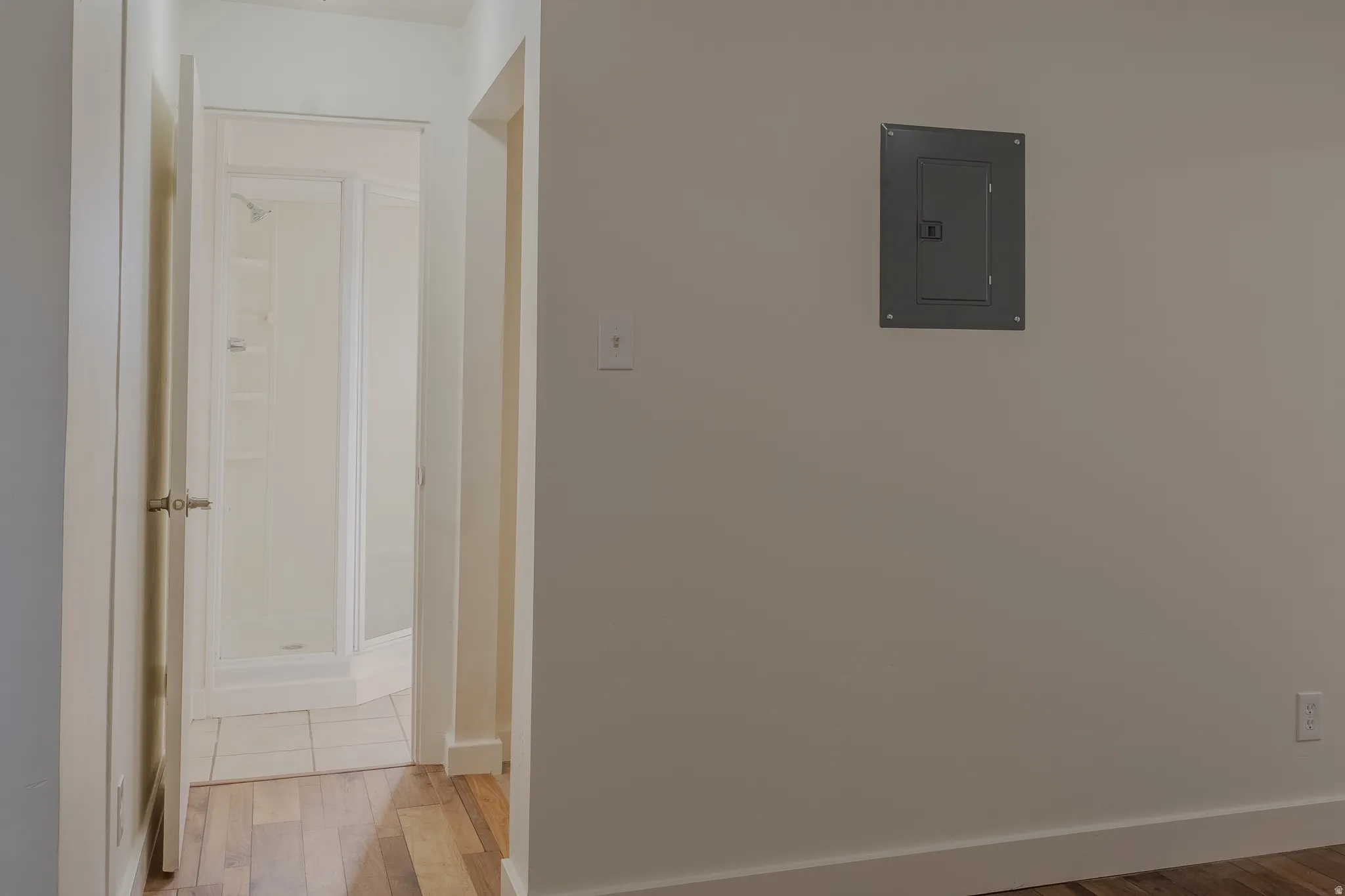 Hallway with wood-finish flooring leading to a bathroom featuring a shower enclosure with frosted glass and white tile flooring