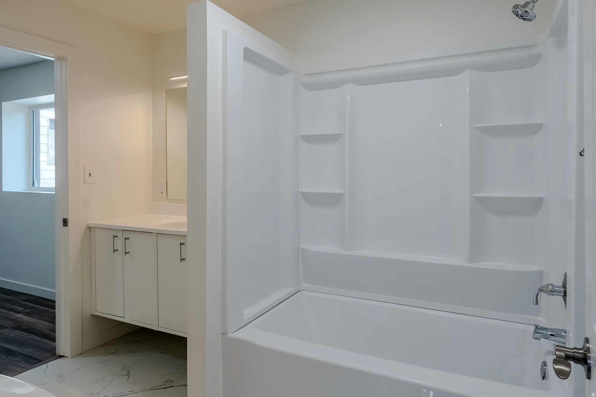 White acrylic tub and shower combination with built-in shelving and chrome fixtures