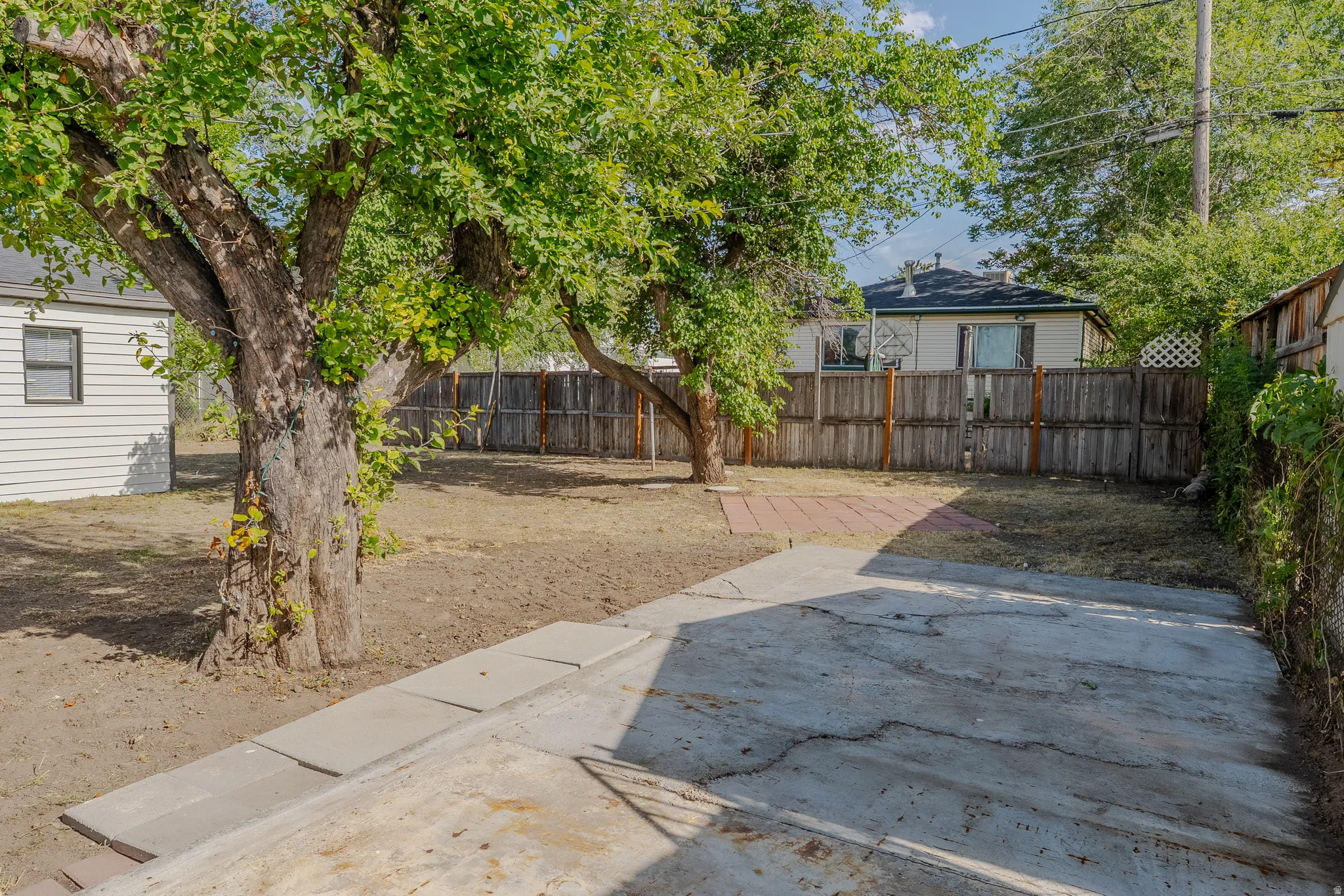 Expansive backyard featuring mature trees, a concrete patio, stepping stones, and a wood fence