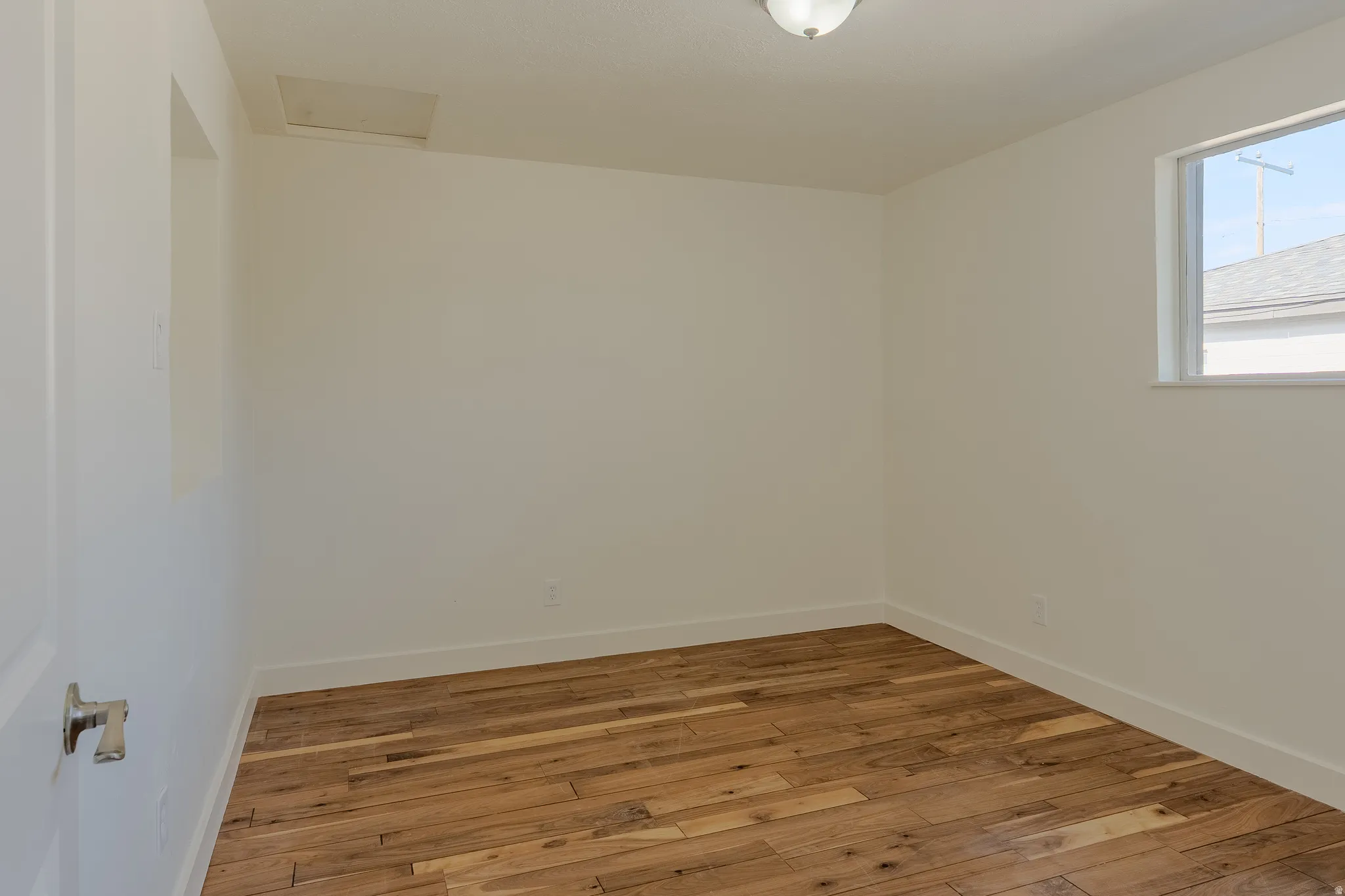 Room with wood-finish flooring, white walls, and a window with white trim