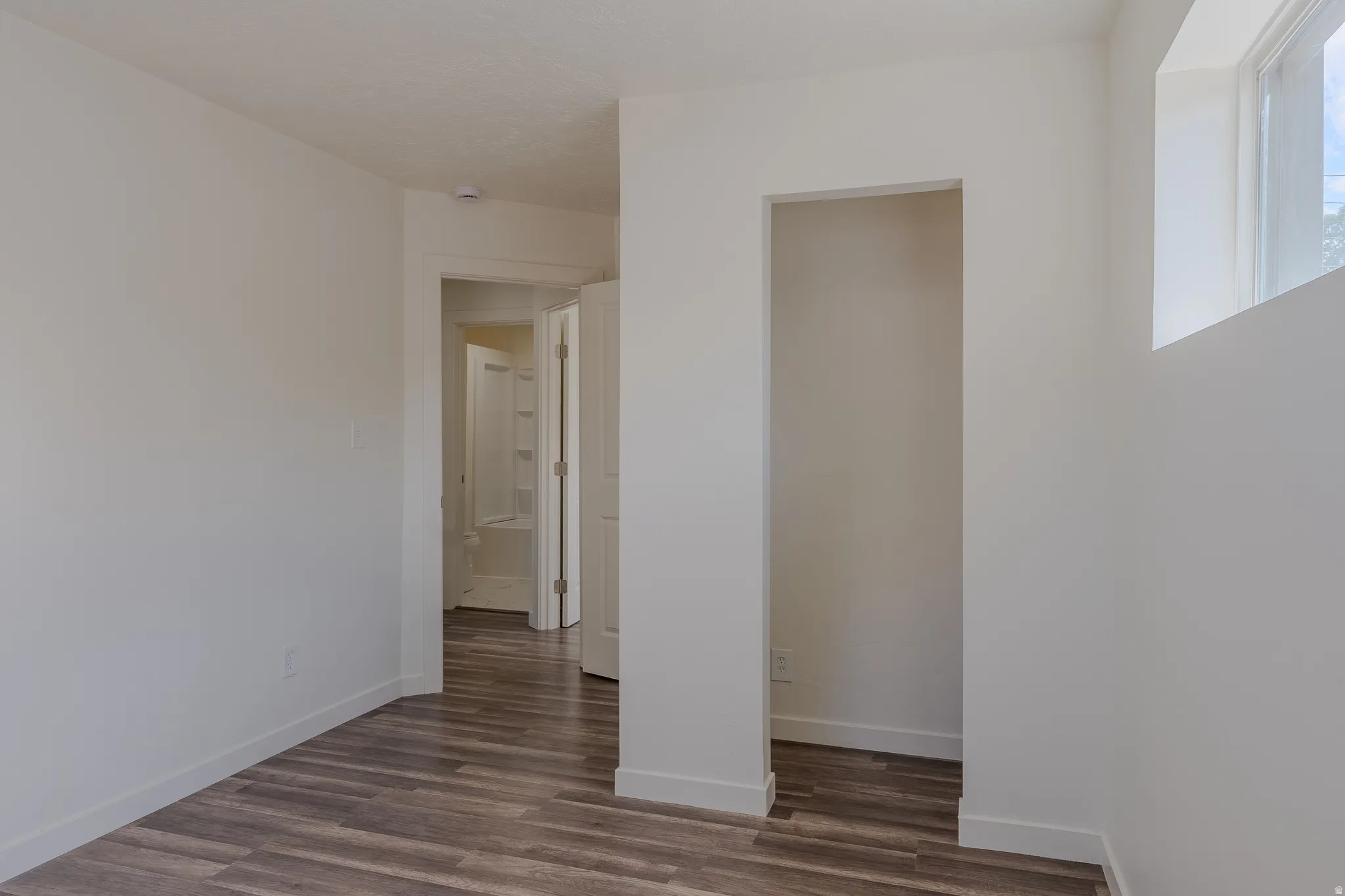 Room with wood-finish flooring, white baseboards, and a window providing natural illumination