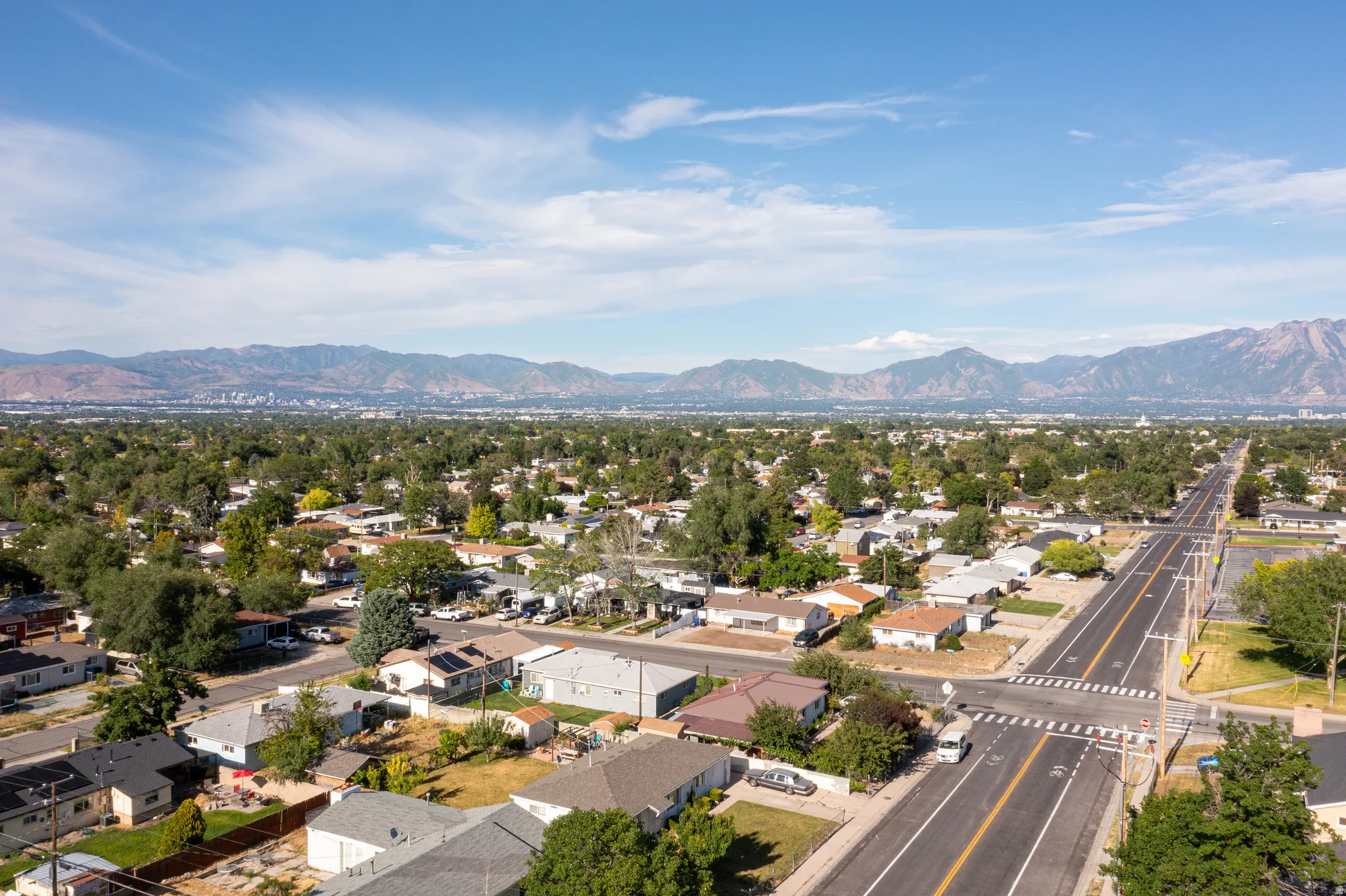 Expansive aerial perspective showcasing a residential area with mature tree coverage, wide roadways, and distant mountain ranges